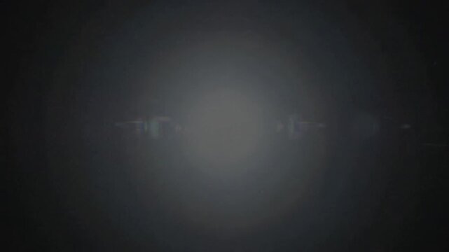 Bright light flare expanding across a dark black background with lens flare effects and negative space for text placement