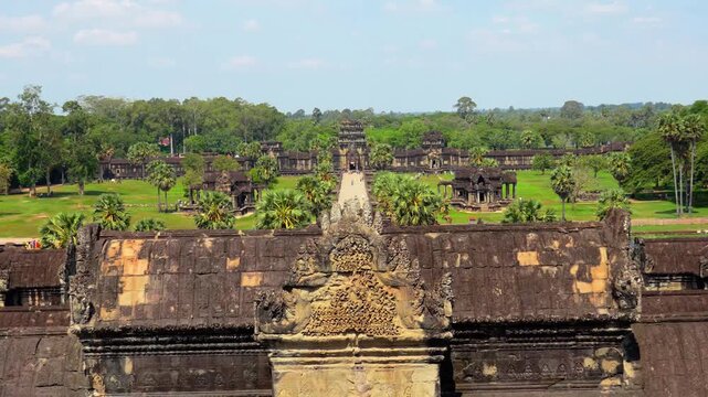 Cinematic view from inside Angkor Wat temple framed by an ancient stone window, overlooking the historic Khmer temple complex and lush tropical landscape in Siem Reap, Cambodia. Stunning footage of