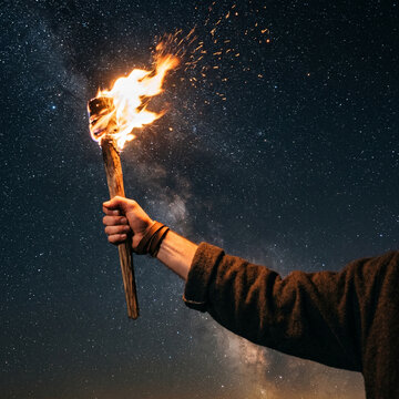 Hand holding burning torch against starry night sky, adventure and discovery concept