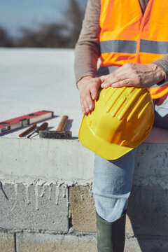 Construction worker working outdoors on a construction site, making a pause and holding a yellow hardhat.