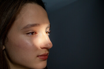 Side profile portrait of teenage girl illuminated by warm sunlight through window blinds against dark background. Concept of confidence, self identity, natural beauty, authentic portrait photography © Ina