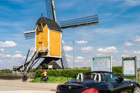 Netherlands, Limburg - April 4, 2023: A luxury BMW convertible parked near an old wooden mill and outdoor tourist displays with travel route maps in Limburg, selective focus