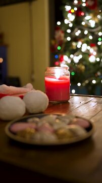 Red burning candle on a wooden table with cookies and a decorated christmas tree in the background