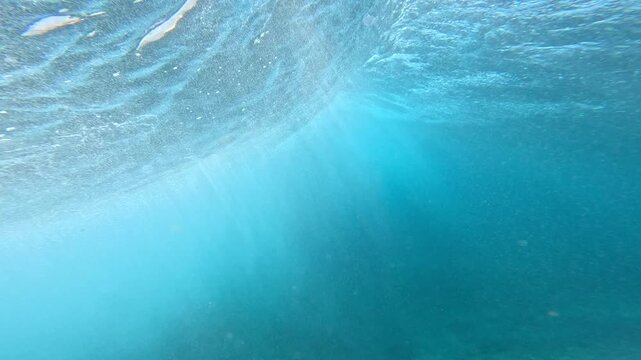 UNDERWATER: Sunlit blue water with swirling bubbles and whitewater glows under a collapsing wave. Pristine beauty, movement and texture of a tropical reef break in surfing mecca of Mentawai Islands.