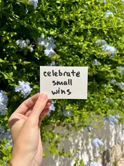 Fototapeta premium Celebrate small wins - hand with motivational card and blue flowers in background, self growth 