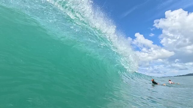 SLOW MOTION: Towering turquoise wave rises over two surfers in the lineup at a remote Mentawai surf spot in Indonesia. Male athletes make a duck dive beneath a wave that breaks in glassy conditions.