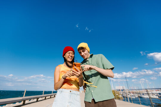 Young friends enjoying social media on smartphone at marina