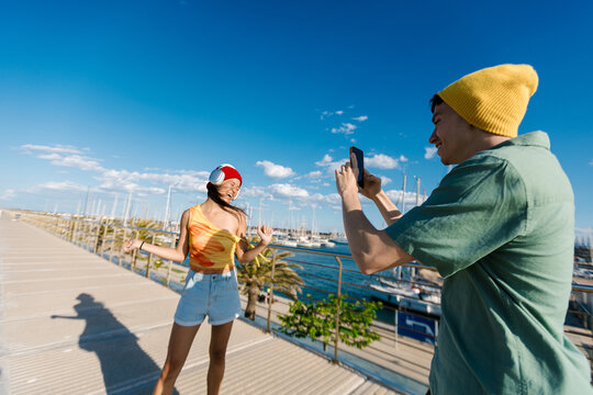 Friends filming cheerful woman dancing by marina