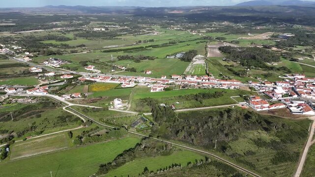 Aerial drone footage panning left over the charming village of Rogil in Portugal, showcasing its houses nestled amidst lush green fields and rolling hills. Part of the beautiful Fisherman's Trail.