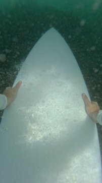 VERTICAL, FPV, SLOW MOTION: Surfer pushes white surfboard down during a duck dive beneath a breaking wave. Practical technique for returning to the lineup while surfing in tropical Mentawai Islands.