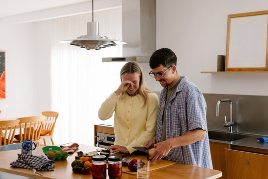 A cheerful couple laughs while slicing fresh vegetables together.