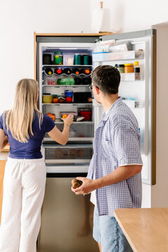 A couple peers into a well-stocked, open fridge in the kitchen.