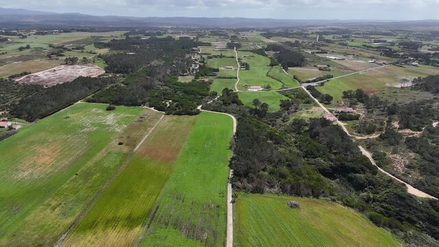 Push in aerial shot of lush green landscapes and fields in rural Portugal near Odeceixe. Part of the Rota Vicentina and Fisherman's Trail, featuring scattered houses and winding dirt paths.