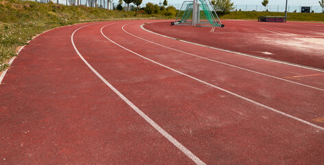 Fototapeta premium Close shot of a red tartan track with white markings on an outdoor sports field. Track for training and competitions. Leisure activity, sports facility, soccer field.