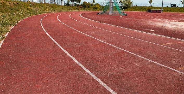 Close shot of a red tartan track with white markings on an outdoor sports field. Track for training and competitions. Leisure activity, sports facility, soccer field.