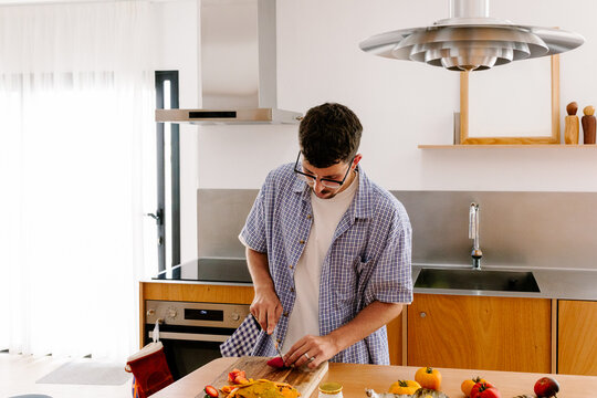 A man in a plaid shirt carefully slices food on a cutting board.