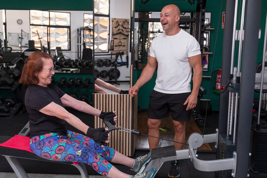 Senior woman and personal trainer smiling on rowing machine