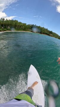 VERTICAL, FPV, SLOW MOTION: Rider trimming and carving across a smooth turquoise wave beside a lush tropical beach. Young man sprays and splashes water while surfing in the scenic Mentawai Islands.