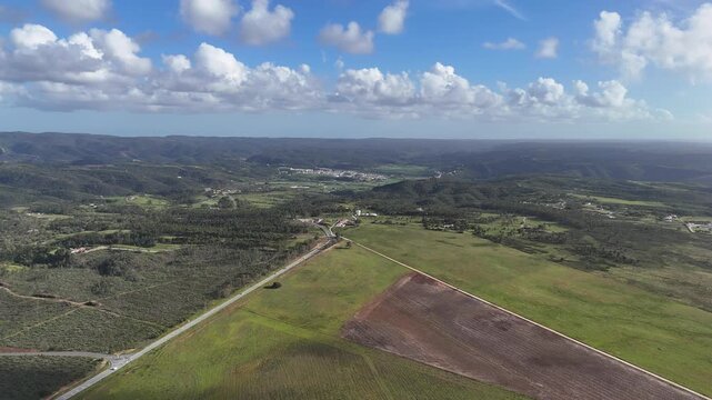 Aerial drone shot pushing in over the beautiful, lush green landscape of Portugal, towards Aljezur. Views of rolling hills, fields, and a road. Part of the Rota Vicentina, Fisherman's Trail region.