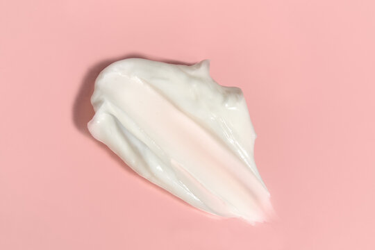 White cosmetic cream smear texture on pink background close up