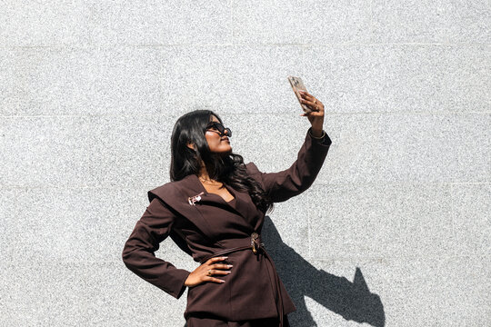 Smiling Indian woman making selfie against grey wall background.