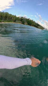 VERTICAL, FPV: Smooth surfing and splashing turns on a peeling wave near tropical coastline. Spraying water, sun, turquoise sea and riding surfboard on long glassy waves at remote Indonesian surf spot