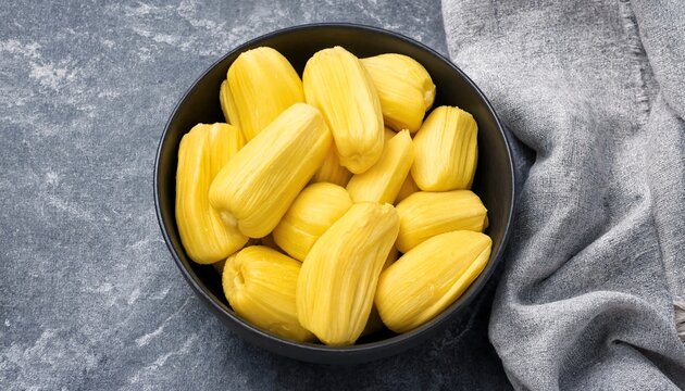 Fresh yellow jackfruit bulbs arranged in a black bowl on a rustic stone background