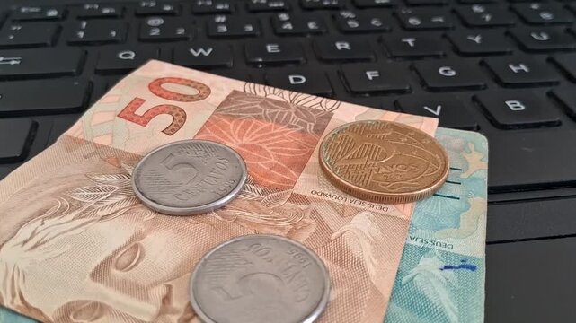Brazilian real banknotes and metal coins resting on laptop motion footage