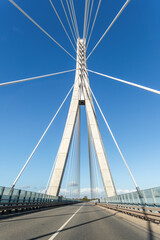 Fototapeta premium Cable bridge in Germany shows concrete pylon, steel cables, empty road, and clear blue sky. Symmetrical perspective creates industrial background for engineering, infrastructure, travel, transport