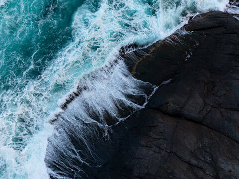 Aerial view of waves crashing against dark coastal rocks