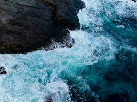 Turquoise waves crashing against dark coastal rocks