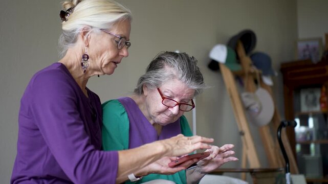 Mature daughter arrives at senior care facility to spend time with her elderly mother, sharing photos and talking together.