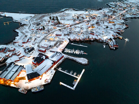 Snow covered coastal harbor village with illuminated docks and boats at dusk
