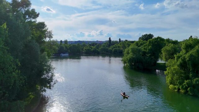 Lone Kayaker Paddling on Calm City Lake Surrounded by Green Trees