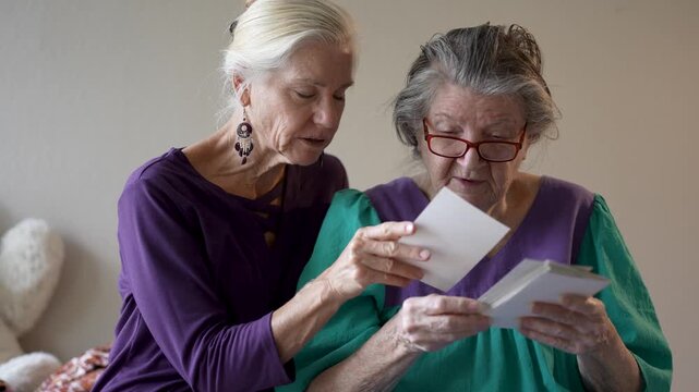 Mature daughter spends time with her elderly mother at a senior care facility talking and sharing old photos and memories together