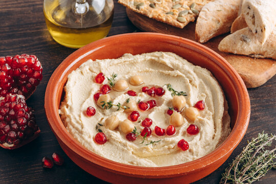 Creamy Hummus With Pomegranate Seeds, Chickpeas, Olive Oil, Pita Bread And Seed Crackers On Wood	