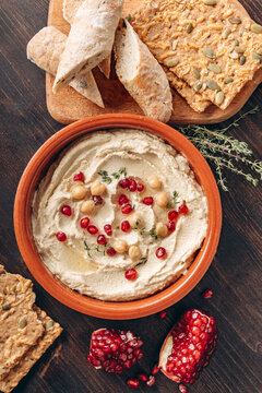 Creamy Hummus With Pomegranate Seeds, Chickpeas, Olive Oil, Pita Bread And Seed Crackers On Wood	