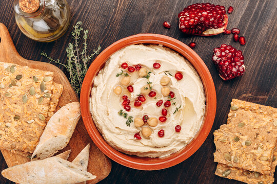Creamy Hummus With Pomegranate Seeds, Chickpeas, Olive Oil, Pita Bread And Seed Crackers On Wood	