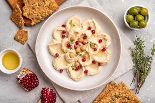 Creamy Hummus With Pomegranate and Crunchy Seed Crackers Served With Olives and Olive Oil