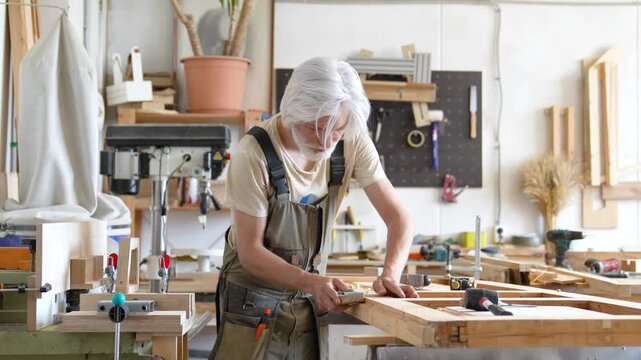 Woodworking and modern restoration workshop settings, professional passionate restorer repairing window frame, precise man crafter sanding frame surface with sandpaper and adjusting with chisel tool.