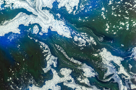 Water flows over rocks in a river with shades of blue and green during daylight