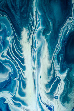 Swirls of blue paint on canvas create a flowing design in an art studio