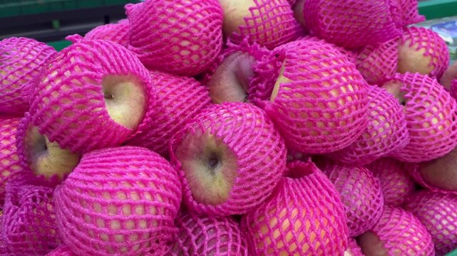 Fresh red apples with pink foam net wrapper heap close up