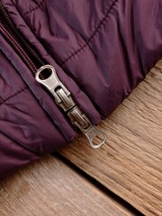 Close up of a metallic two ways zipper on a purple puffer coat. The coat is on a wooden table. © Kati Maria
