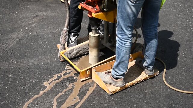 Road worker drilling asphalt core sample for pavement quality inspection