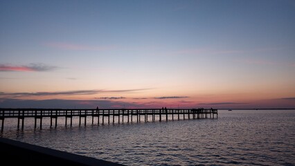 Obraz premium Wooden pier extending into calm water at colorful twilight sunset