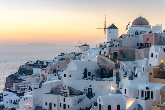 Tourists admire the iconic white houses and windmills of Oia during a scenic sunset.