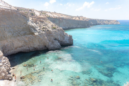 Tourists enjoy swimming in the crystal clear turquoise water at beautiful Tsigrado beach Milos.