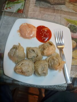 Close up of appetizer dumplings with tomato sauce on white plate with fork on wooden table