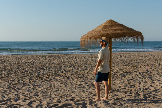 Hispanic man enjoying sunny beach beside straw umbrella